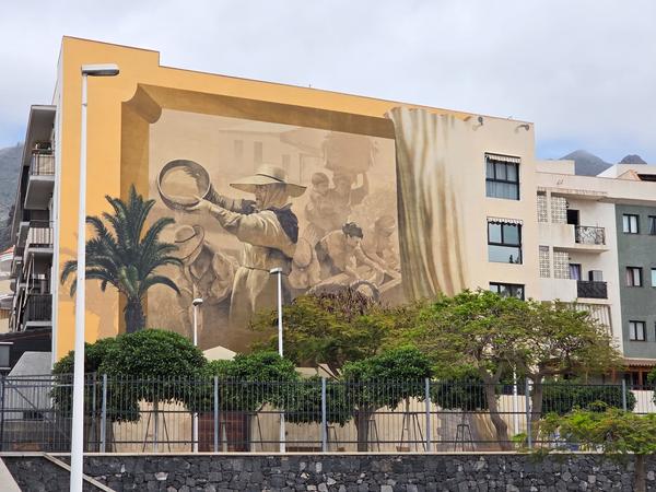 Grande murale che raffigura contadini in una scena agricola tradizionale, su parete di edificio.
