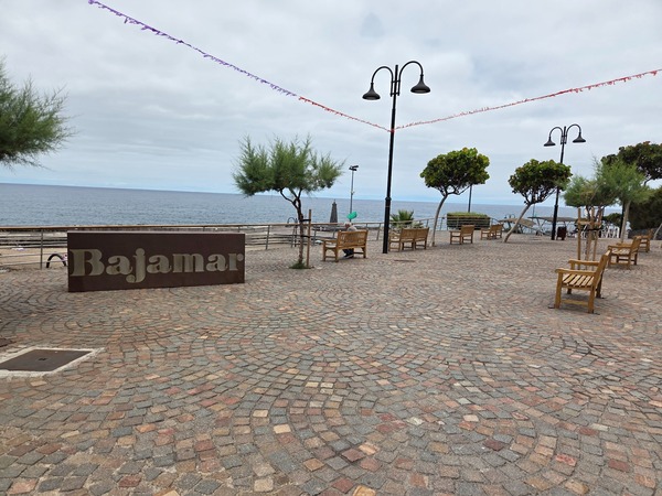 Piazza del lungomare con panchine, alberi e la scritta Bajamar davanti all’oceano.