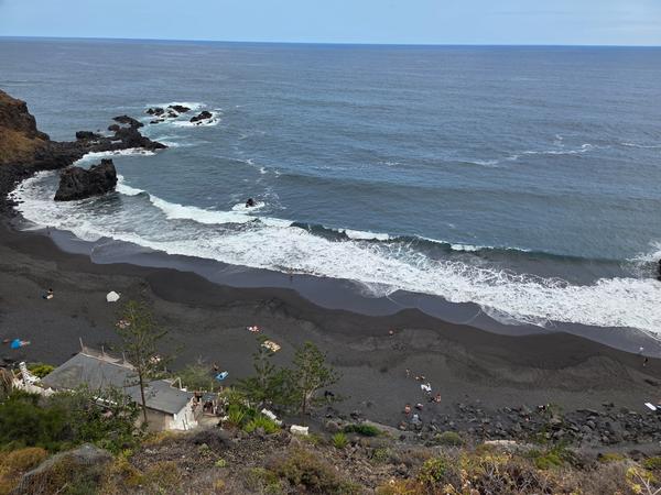 Vista panoramica della Playa del Bollullo dall'alto, con la sabbia nera e le onde dell'oceano che si infrangono sulla riva.
