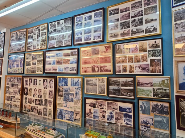 Grandi collage fotografici con immagini storiche di porti, barche e comunità di pescatori esposti alla parete.
