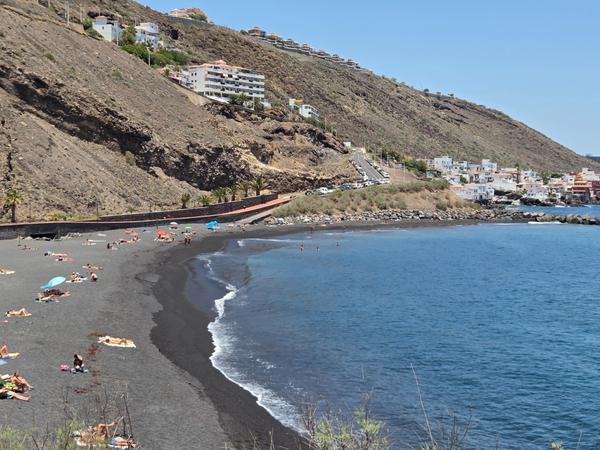 Bagnanti distesi sulla sabbia vulcanica della spiaggia di Nea con vista sul borgo costiero
