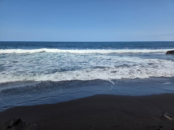 Onde dell’Atlantico che si infrangono sulla spiaggia di sabbia vulcanica nera di Playa El Ancón in una giornata limpida.