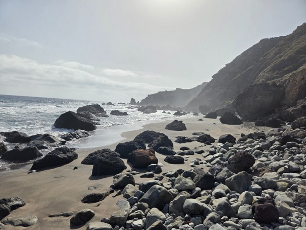 La spiaggia di Las Breñas con scogli vulcanici e i pendii dell’Anaga illuminati dal controluce dell’oceano.