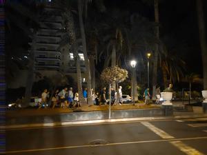 Gruppi di persone camminano lungo i marciapiedi tra palme e lampioni nella notte di San Juan.
