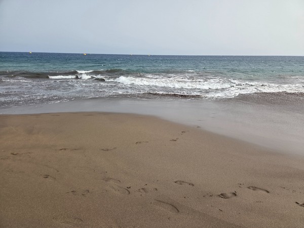 Piccole onde si frangono sulla sabbia scura di La Tejita lasciando impronte e riflessi sulla battigia.