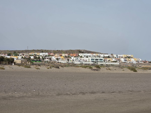 Quartiere residenziale vicino a La Tejita con case basse dai colori pastello e autobus di linea che costeggia la spiaggia.